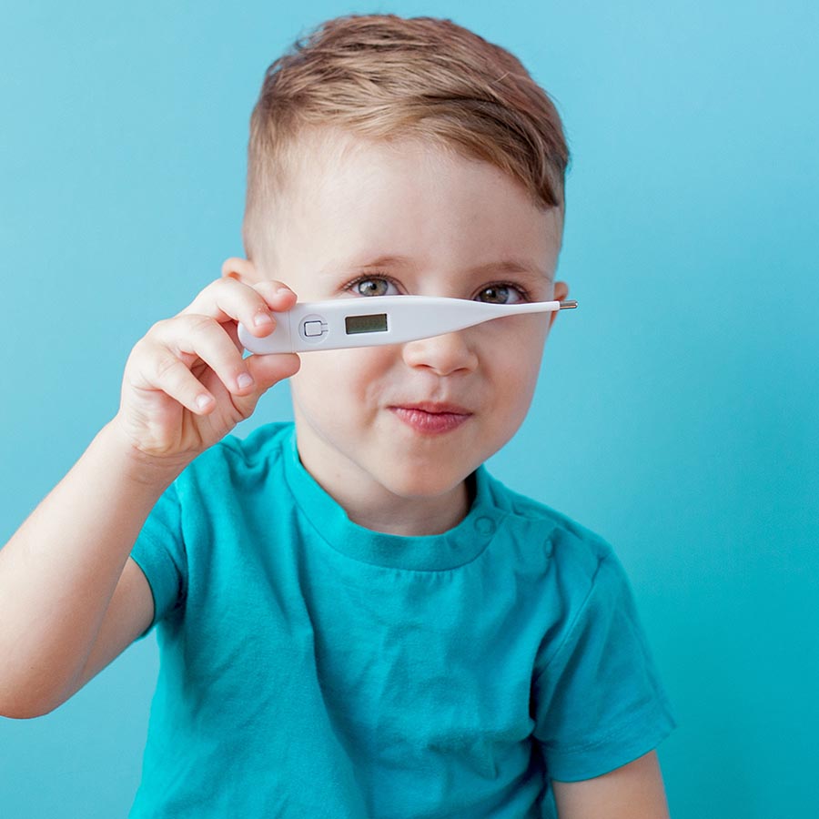 Ill young child with a thermomether, measuring the height of his fever and looking into the camera.